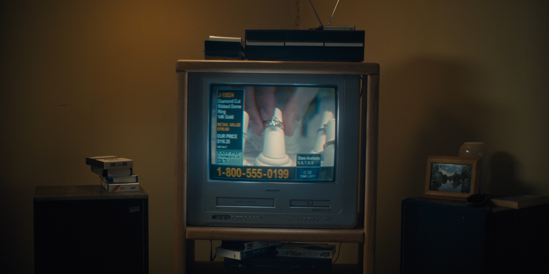 An old CRT television on a wooden stand in a dim room, VHS tapes stacked beside it