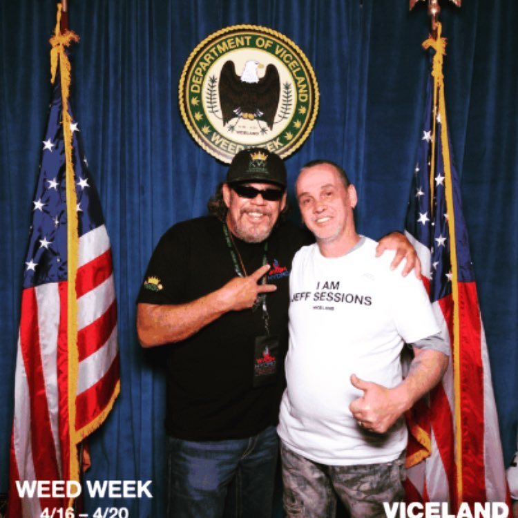 Two men posing in front of a Department of Justice seal backdrop at the Weed Week activation